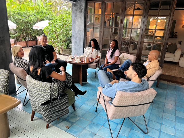 A group in conversation around a low table in a light-filled garden room